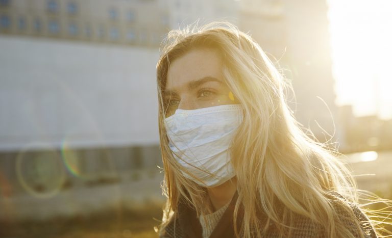 Young woman outside wearing a virus protective face mask as metaphor for the article "COVID-19 still looming large"