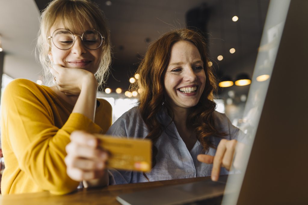 Two happy female friends with laptop and credit card as metaphor for the article "Payments – Made in Germany "Payments – Made in Germany"