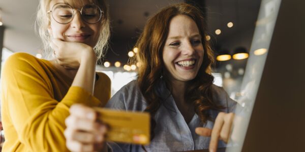 Two happy female friends with laptop and credit card as metaphor for the article "Payments – Made in Germany "Payments – Made in Germany"