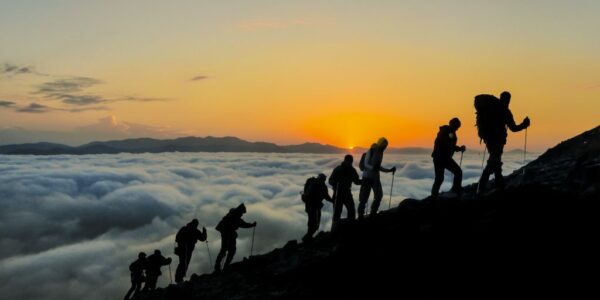 Silhouettes of hikers climbing the mountain at sunset as a metaphor for employee activation